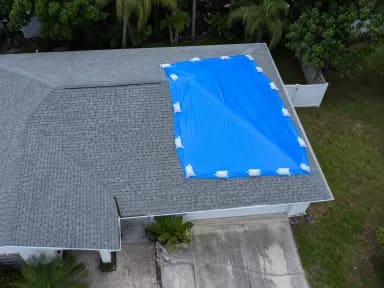 Drone view of a Florida home with a blue emergency tarp staked over a damaged roof section.