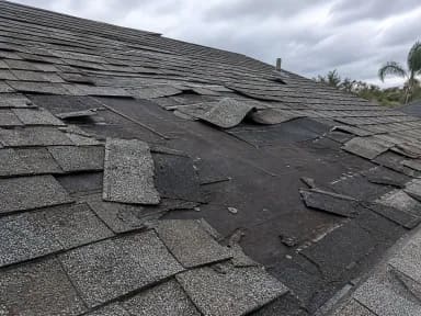 Close-up of storm-damaged shingles with multiple tabs lifted and torn, exposing the underlayment beneath.