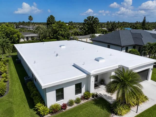 Drone view of a finished white TPO flat roof on a one-story Florida home surrounded by palms.